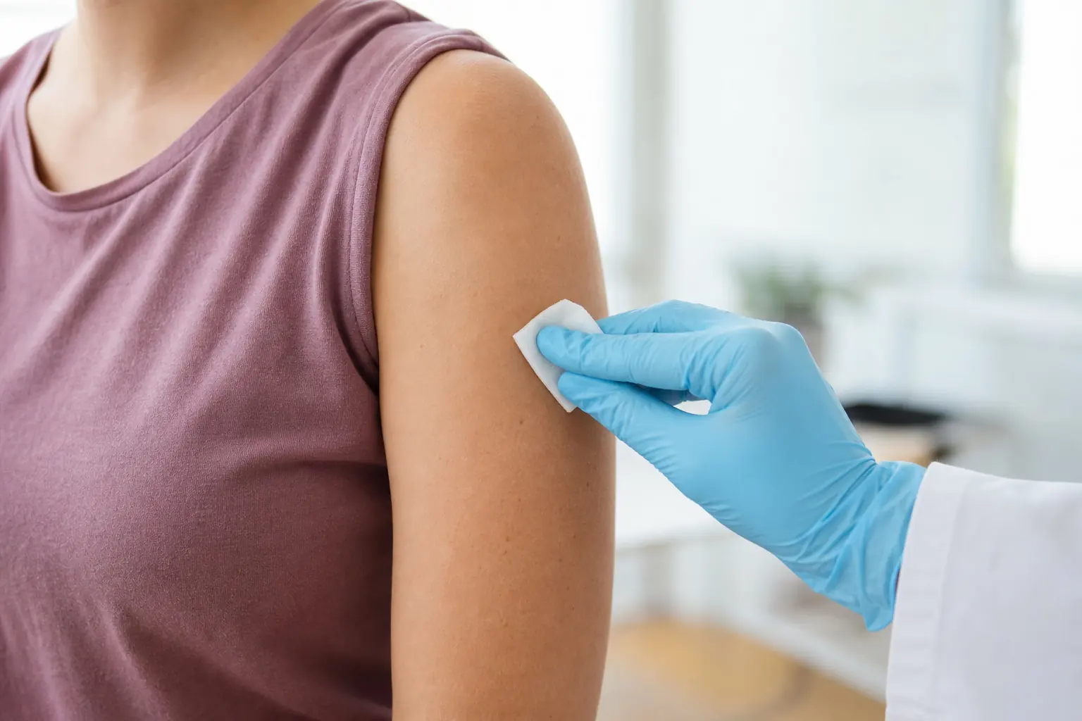 A gloved hand swabbing an upper arm before an injection