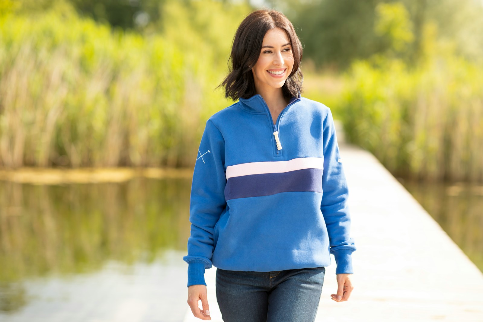 A woman in a blue sweater is walking by a body of water